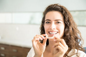 Woman holding a clear aligner for Invisalign.