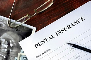 Dental insurance paperwork on desk with glasses, X-rays, and money
